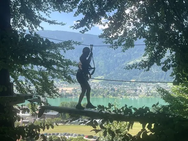 Silhouette einer Person auf dem Kletterwald Ossiachersee hoch über den Bäumen mit Blick auf den türkisen See