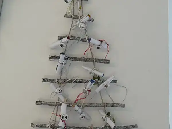 Selbst gebastelter Adventskalender aus Ästen als Tannenbaum an der Wand, mit den Fotoaufgaben-Kärtchen als kleinen Papierröllchen an Bändern aufgehängt