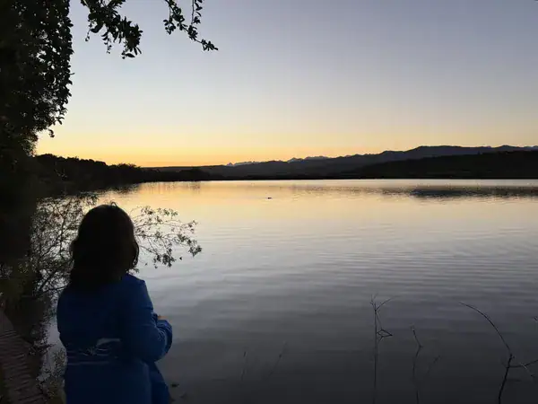 Sonnenuntergang am Wasserloch der Buffelsdrift Game Lodge, im Vordergrund eine Person am Ufer