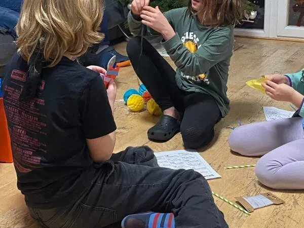 Drei Kinder sitzen am Silvesterabend am Boden und lösen Aufgaben aus den Countdown-Tüten