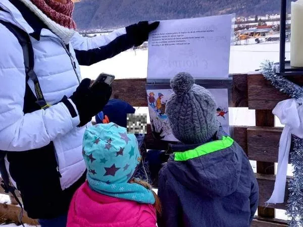 Eine Kindergruppe und eine Erwachsene lesen im Winter bei einer Schnitzeljagd im Freien einen Hinweis